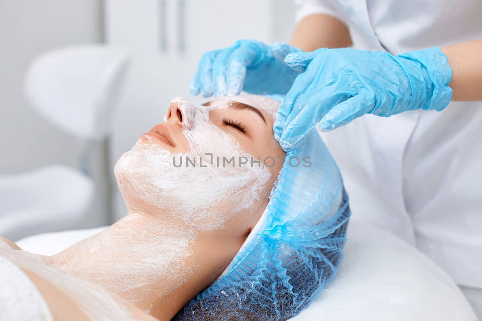 close-up, beautician applies the mask to the face of beautiful young woman in the spa salon. facial skin care concept.