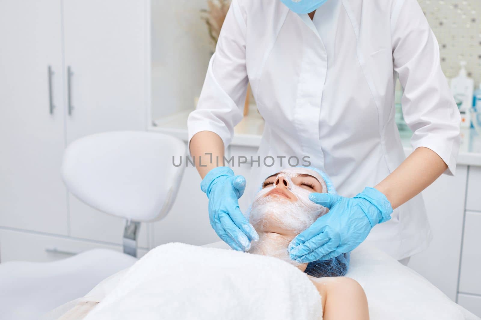 beautician applies the mask to the face of beautiful young woman in the spa salon. facial skin care concept.