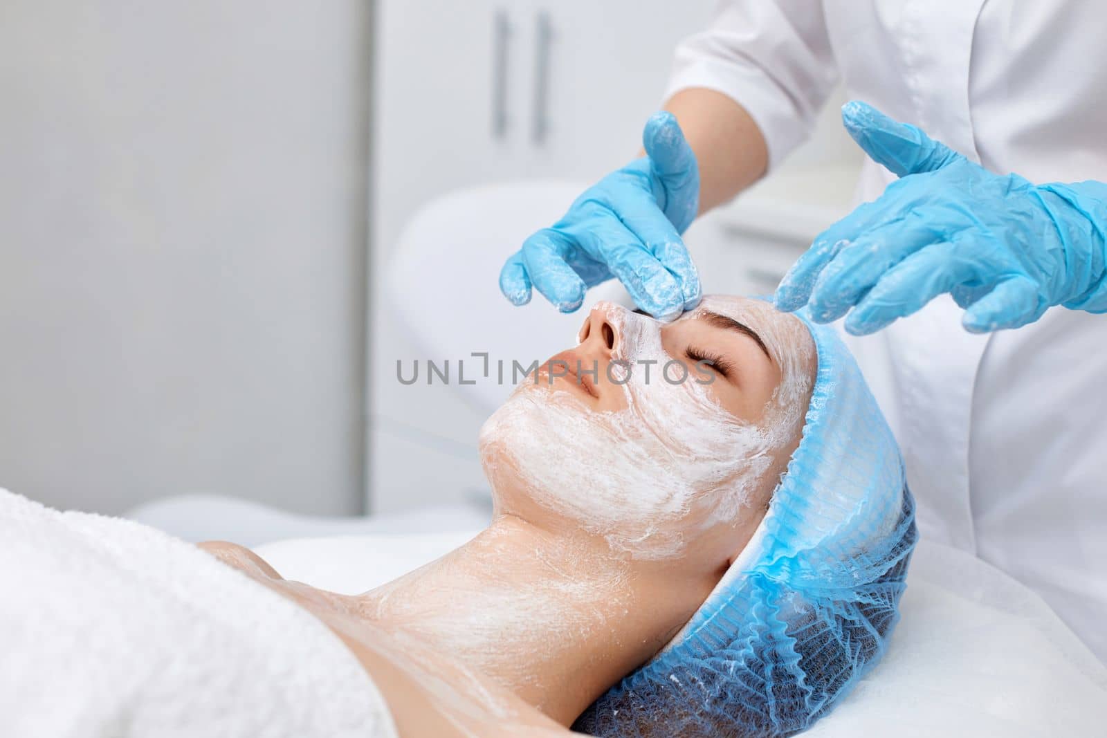 beautician applies the mask to the face of beautiful young woman in the spa salon. facial skin care concept.