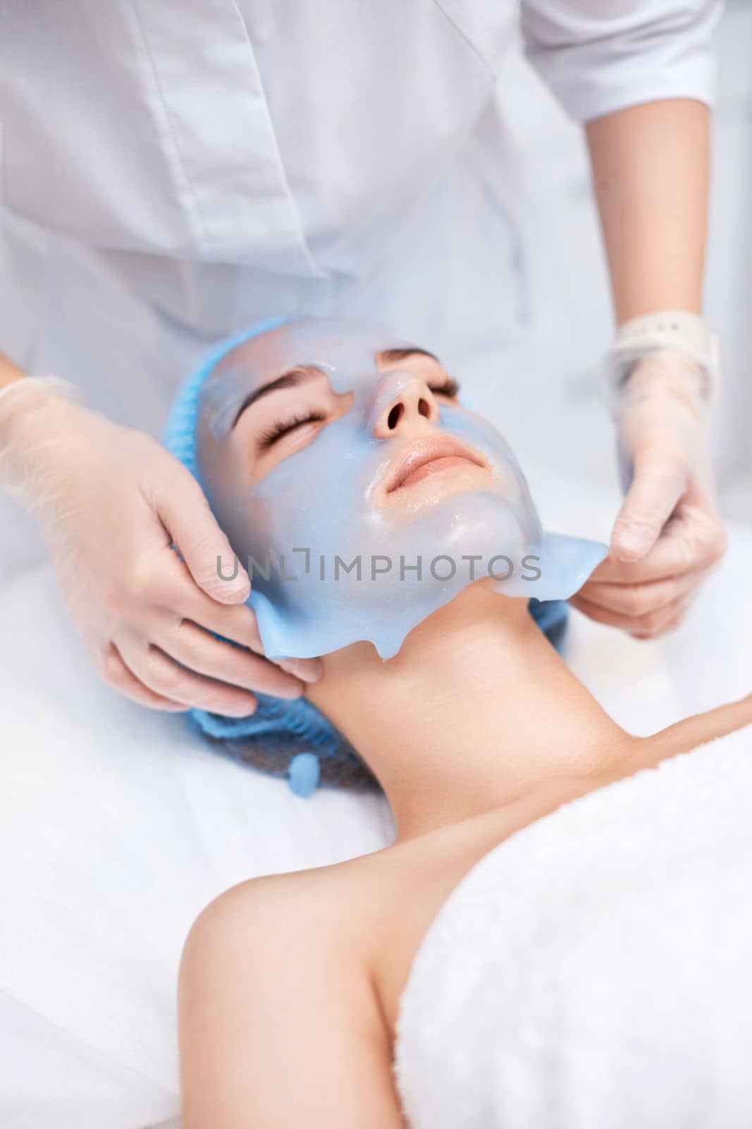beautician removing blue alginate mask from face of beautiful woman in the spa salon. spa treatments
