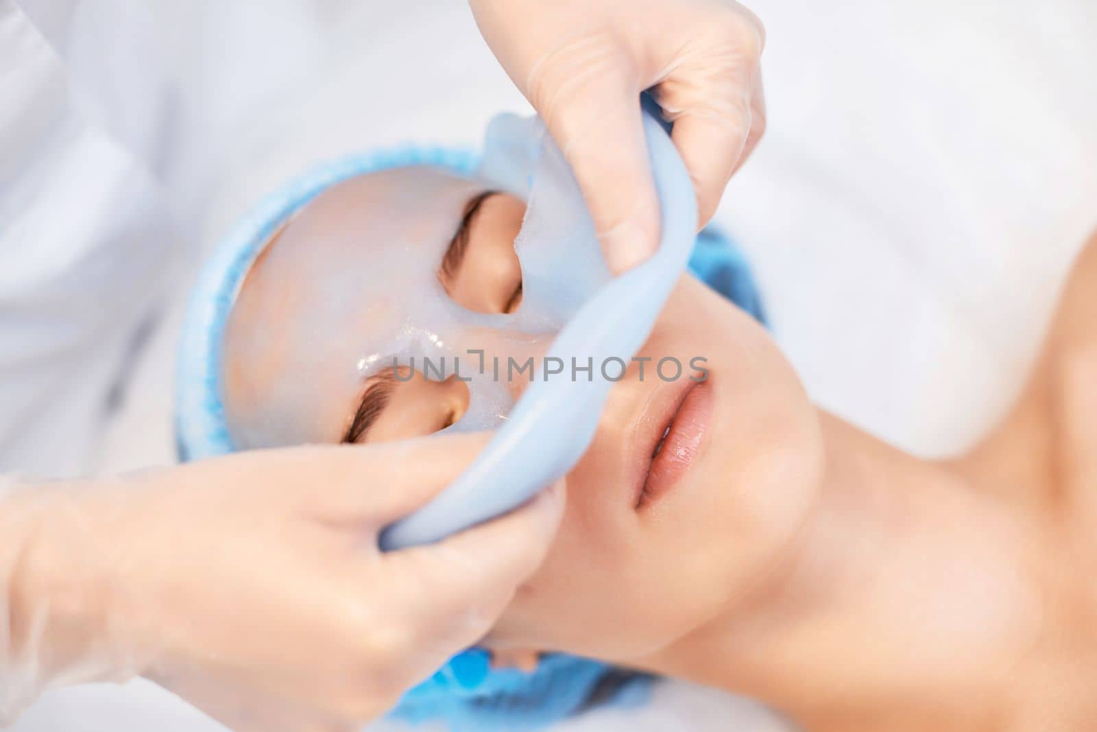 beautician removing blue alginate mask from face of beautiful woman in the spa salon. spa treatments