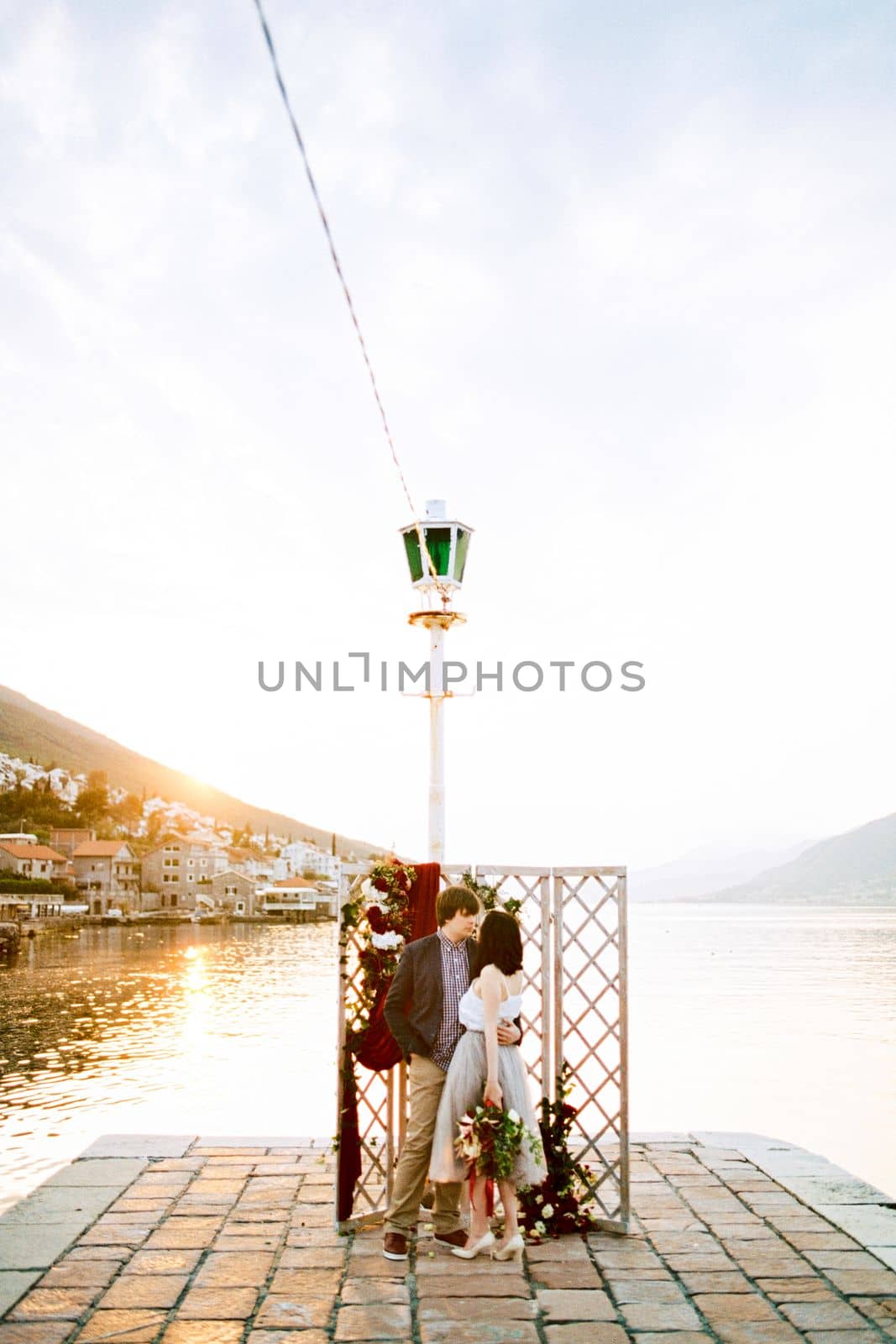 Bride and groom stand hugging near the wedding screen on the pier by the sea. High quality photo