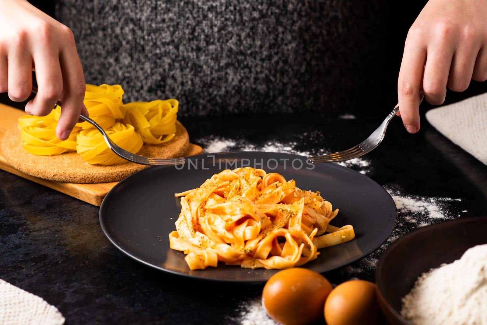 A close-up of hands holding fork, digging into a plate of fast food in a kitchen.