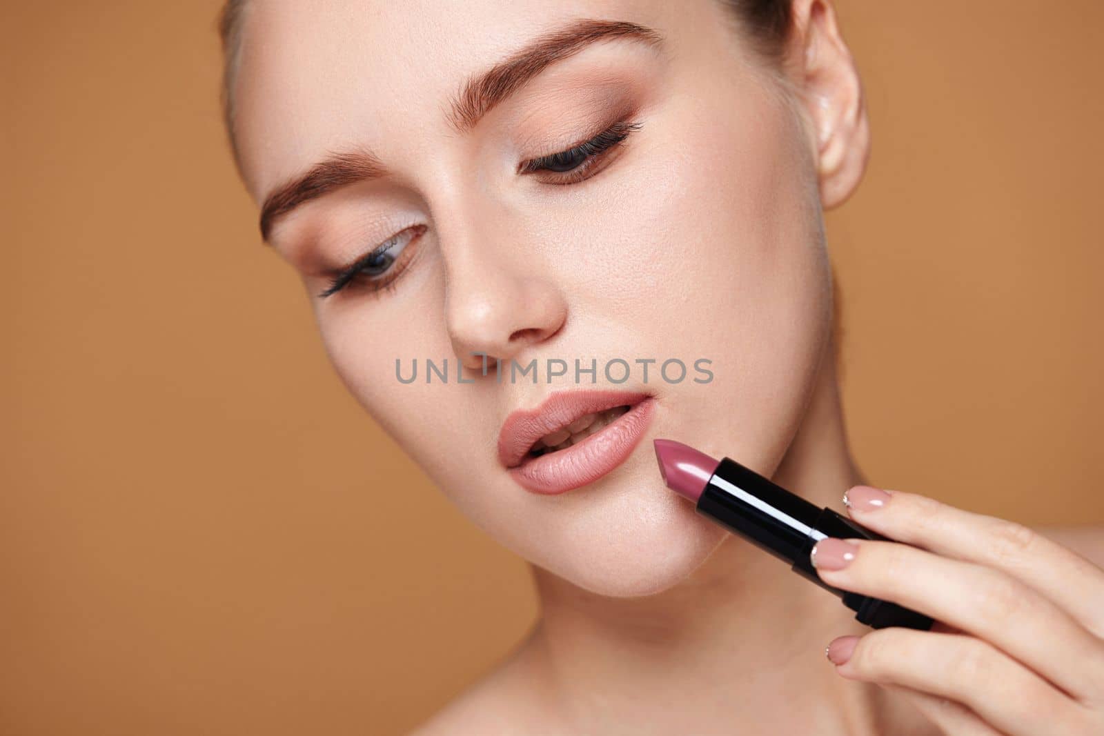 beautiful woman applying pink lipstick on beige background, close-up