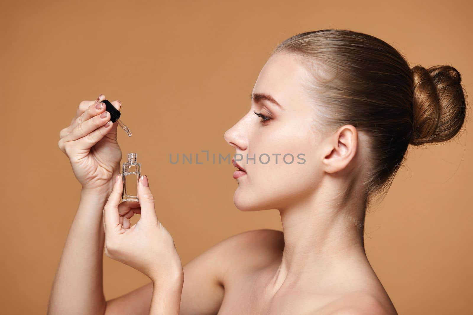 attractive woman holding bottle with serum for skin care on beige background