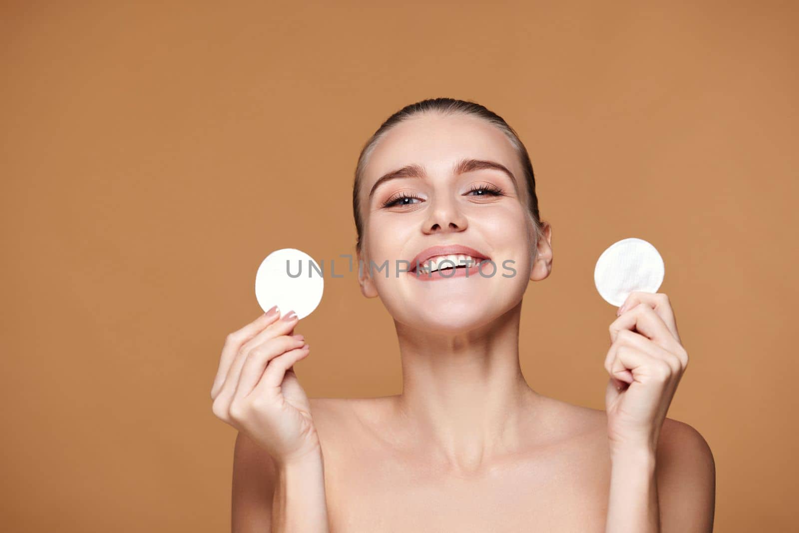 very excited laughing young woman holding two white cotton disks pad with micellar water on beige background