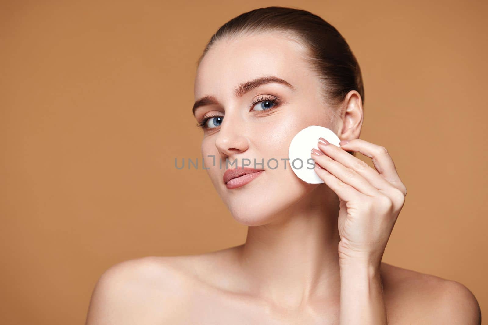 young woman holding white cotton pad with micellar water on beige background