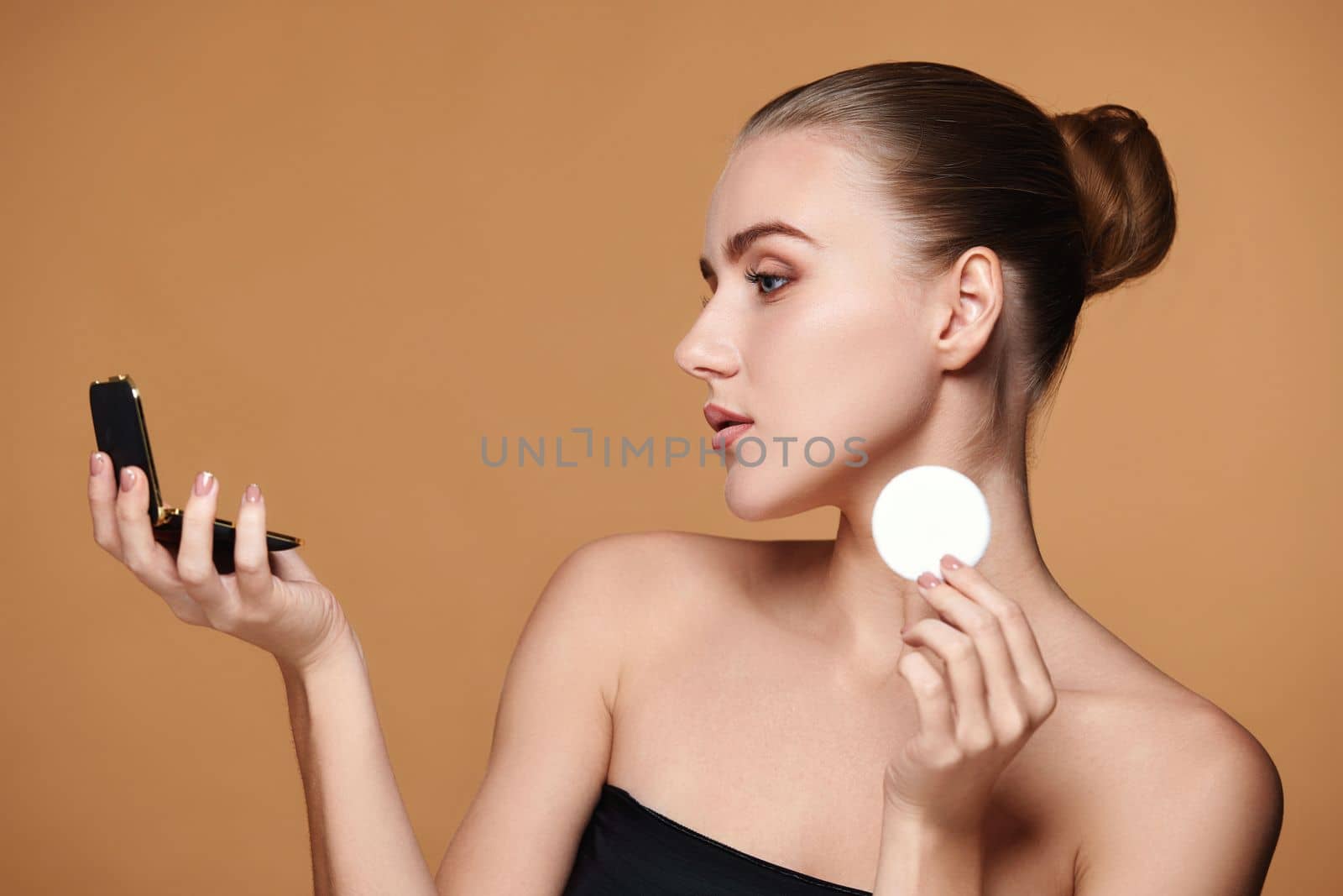 beautiful woman look at mirror and holding white cotton pad for removing makeup on beige background