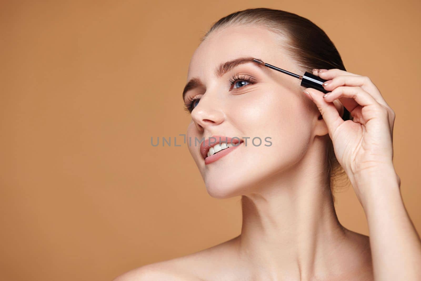 Beautiful happy woman with perfect shape eyebrows on beige background. Natural make up. copy space