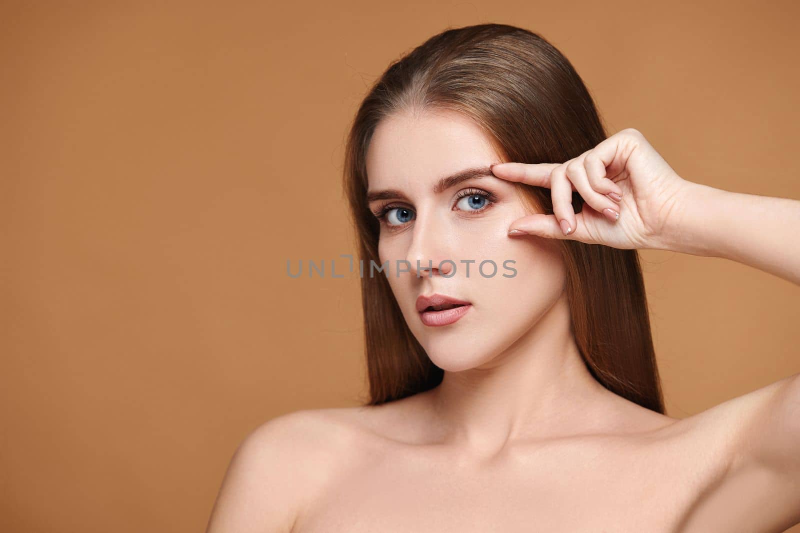 Beautiful healthy woman with perfect skin check the line of eyebrows and eyes without wrinkles on beige background. Face lifting concept.