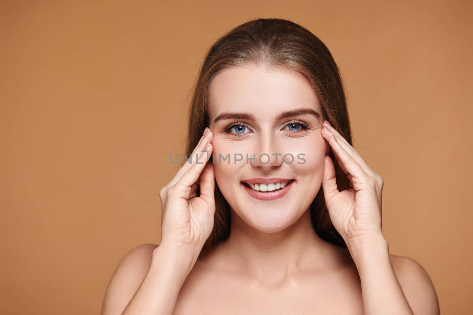 Beautiful woman with long hair and perfect clean skin touching face on beige background