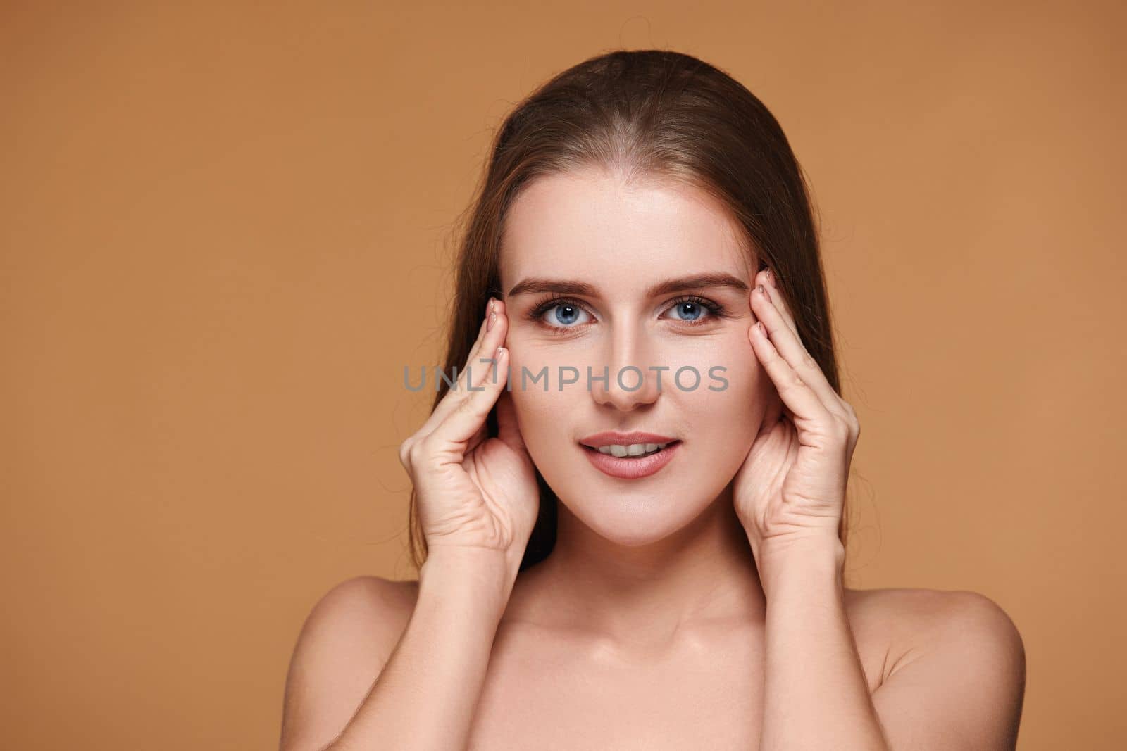 Beautiful woman with long hair and perfect clean skin touching face on beige background