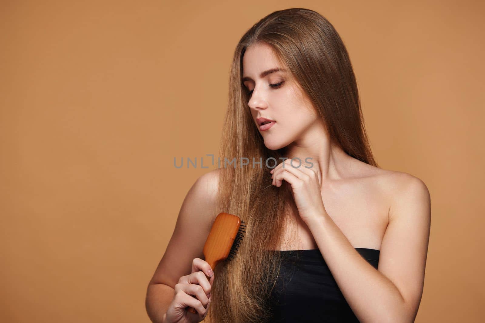brunette woman combs her long natural hair with wooden brush on beige background