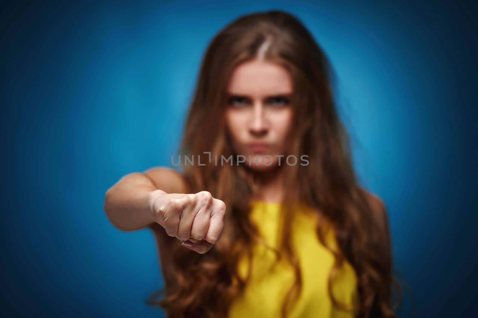 Ukrainian woman in yellow t-shirt protesting against Russian military invasion in Ukraine on blue background. Angry gesture. focus on fist