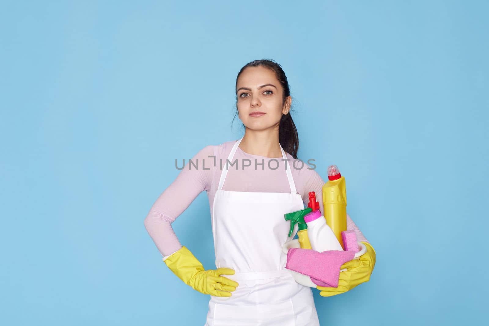 pretty caucasian woman in gloves holding bucket with cleaning supplies isolated on blue background.
