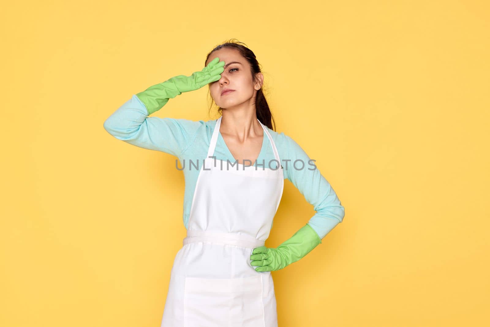 tired woman in gloves and cleaner apron on yellow background
