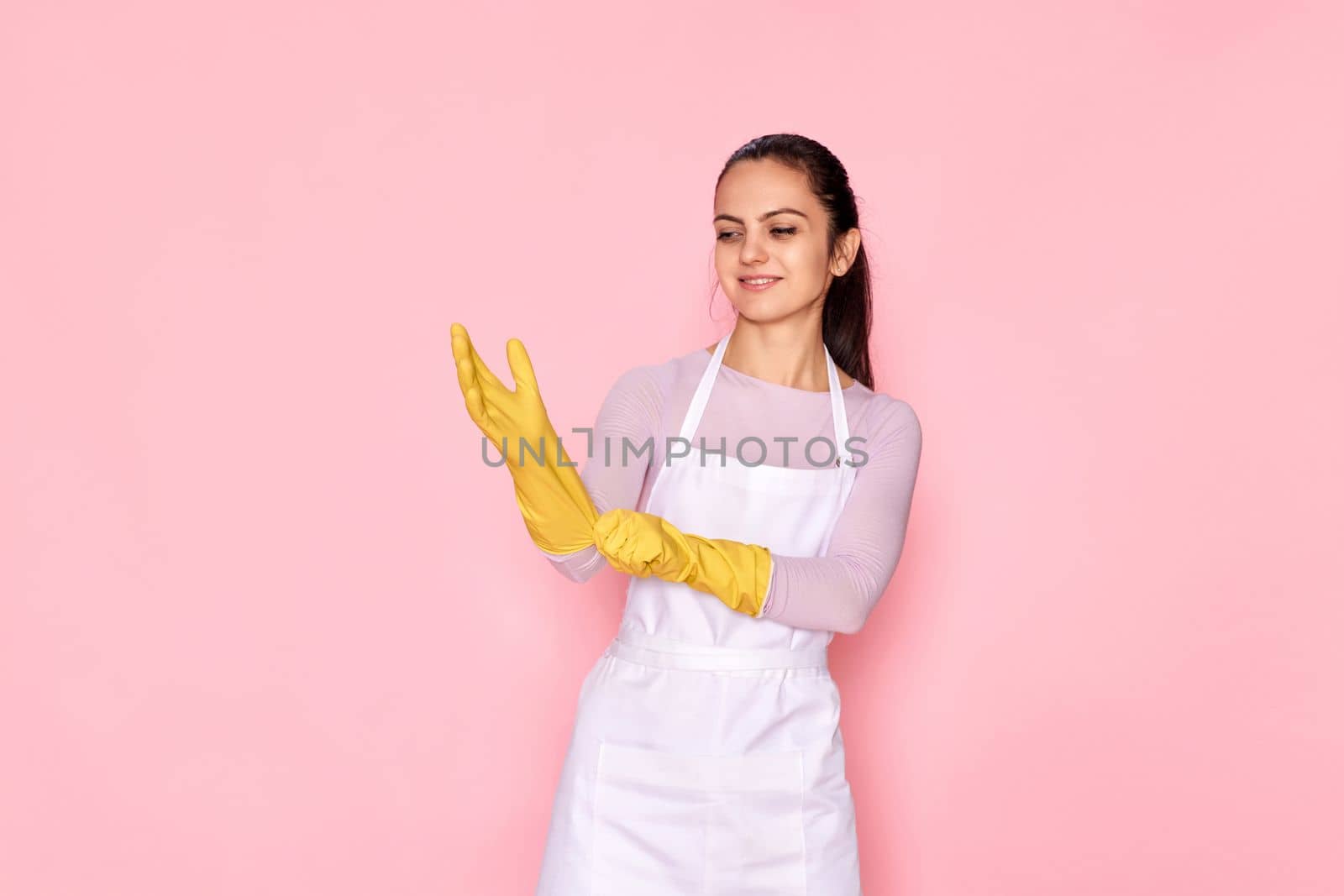 happy caucasian woman wearing yellow rubber gloves on pink background.