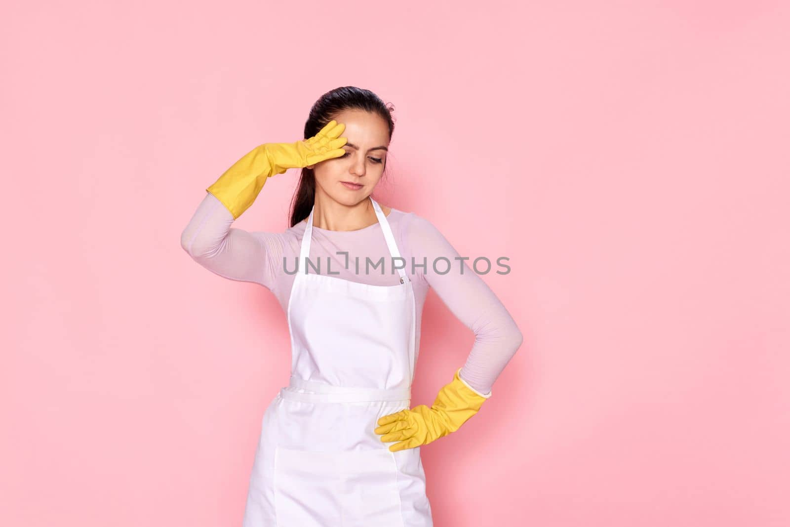 tired woman in gloves and cleaner apron on pink background