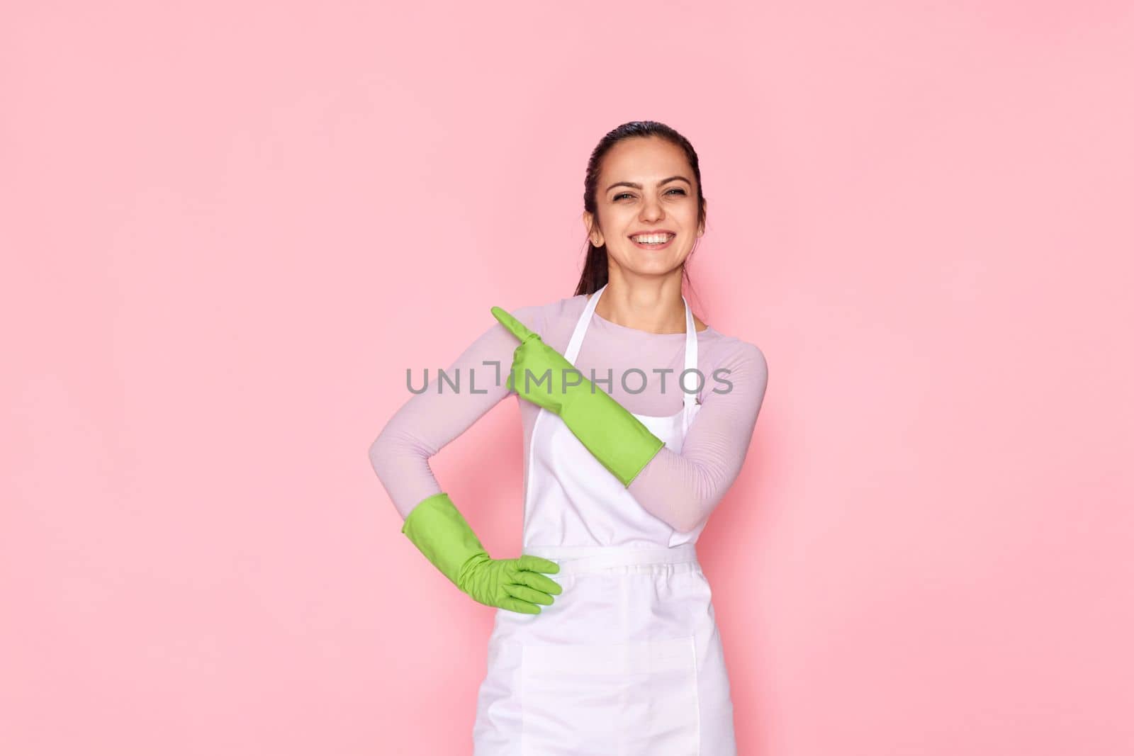 beautiful caucasian woman in rubber gloves pointing fingers aside at copy space on pink background. cleaning