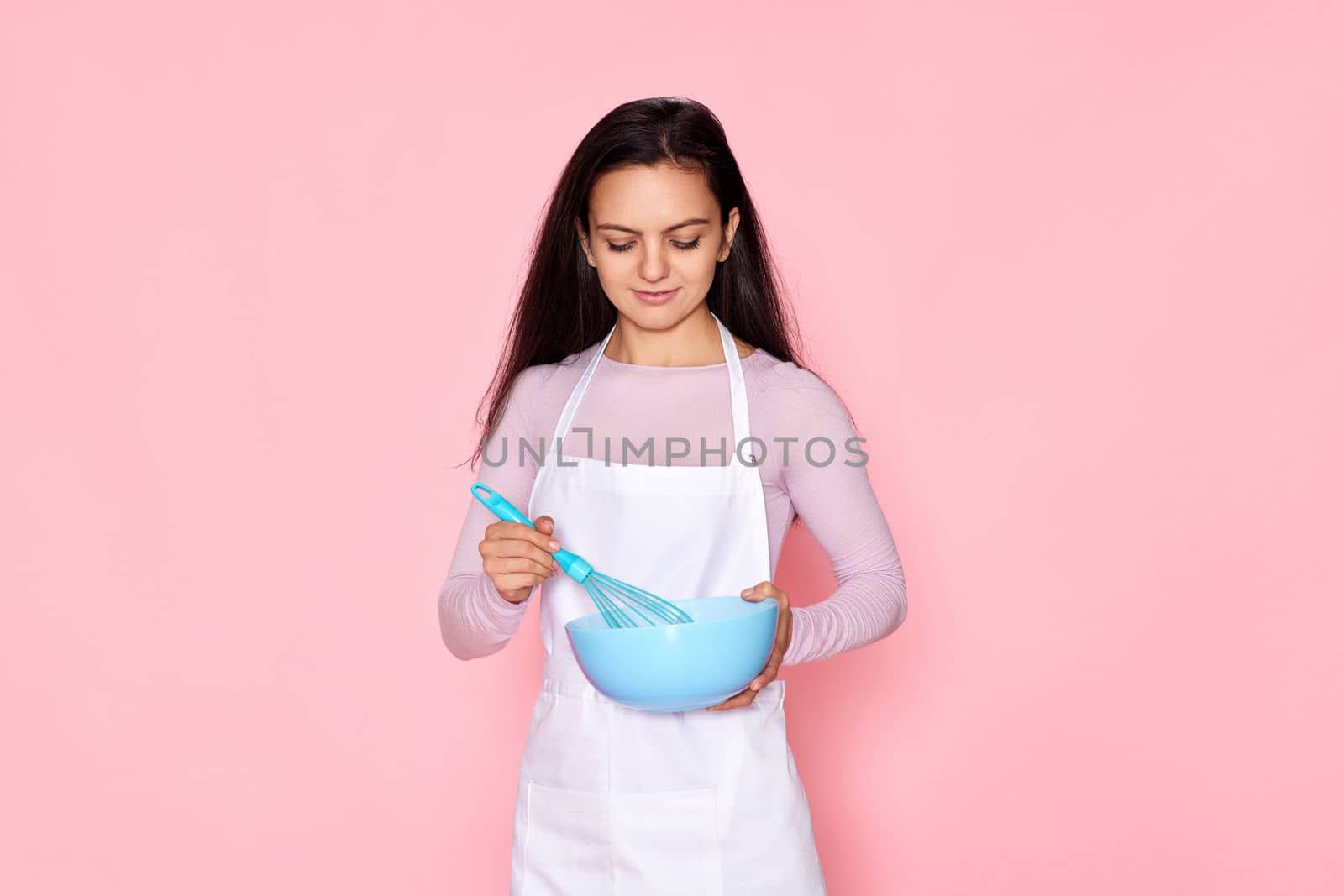 Pretty cooker woman holding whisk and bowl on pastel pink background