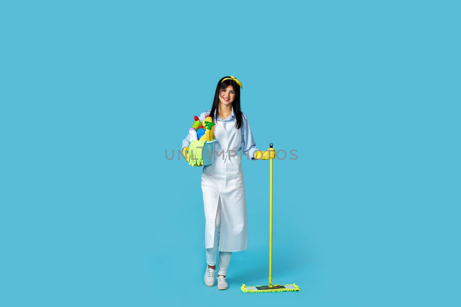 professional cleaner woman in rubber gloves and cleaner apron with cleaning supplies and mop on blue background