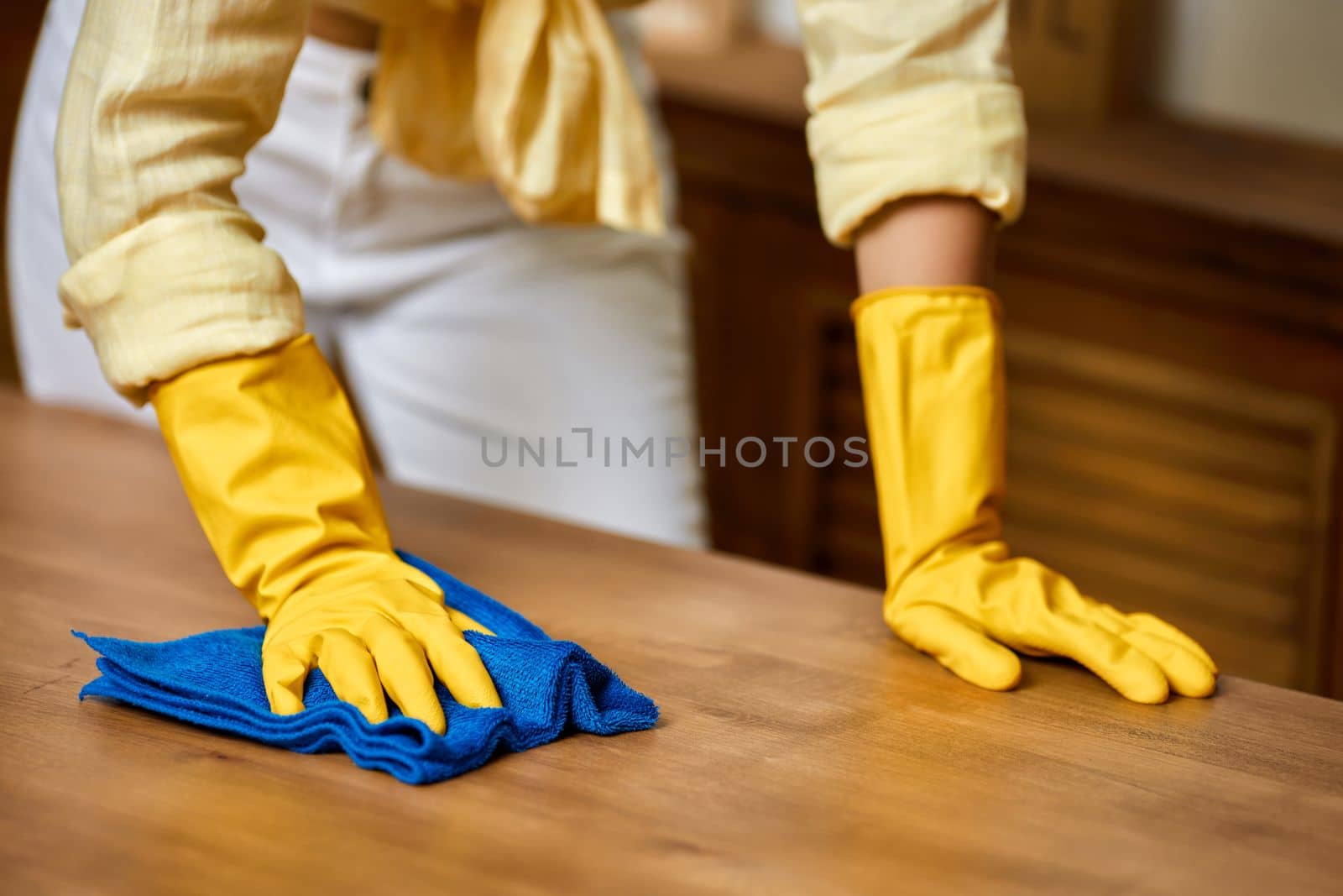 brunette woman in yellow gloves using a rag while cleaning furniture at home