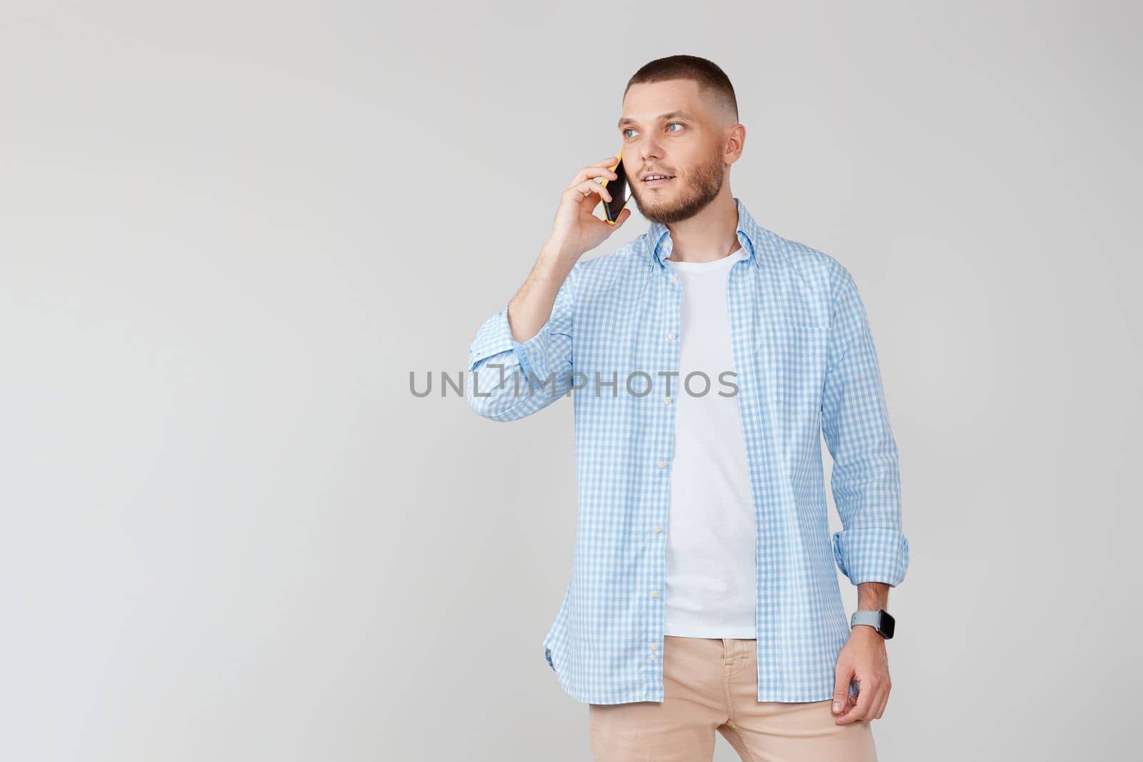 Handsome young man using cell phone while standing against gray background.
