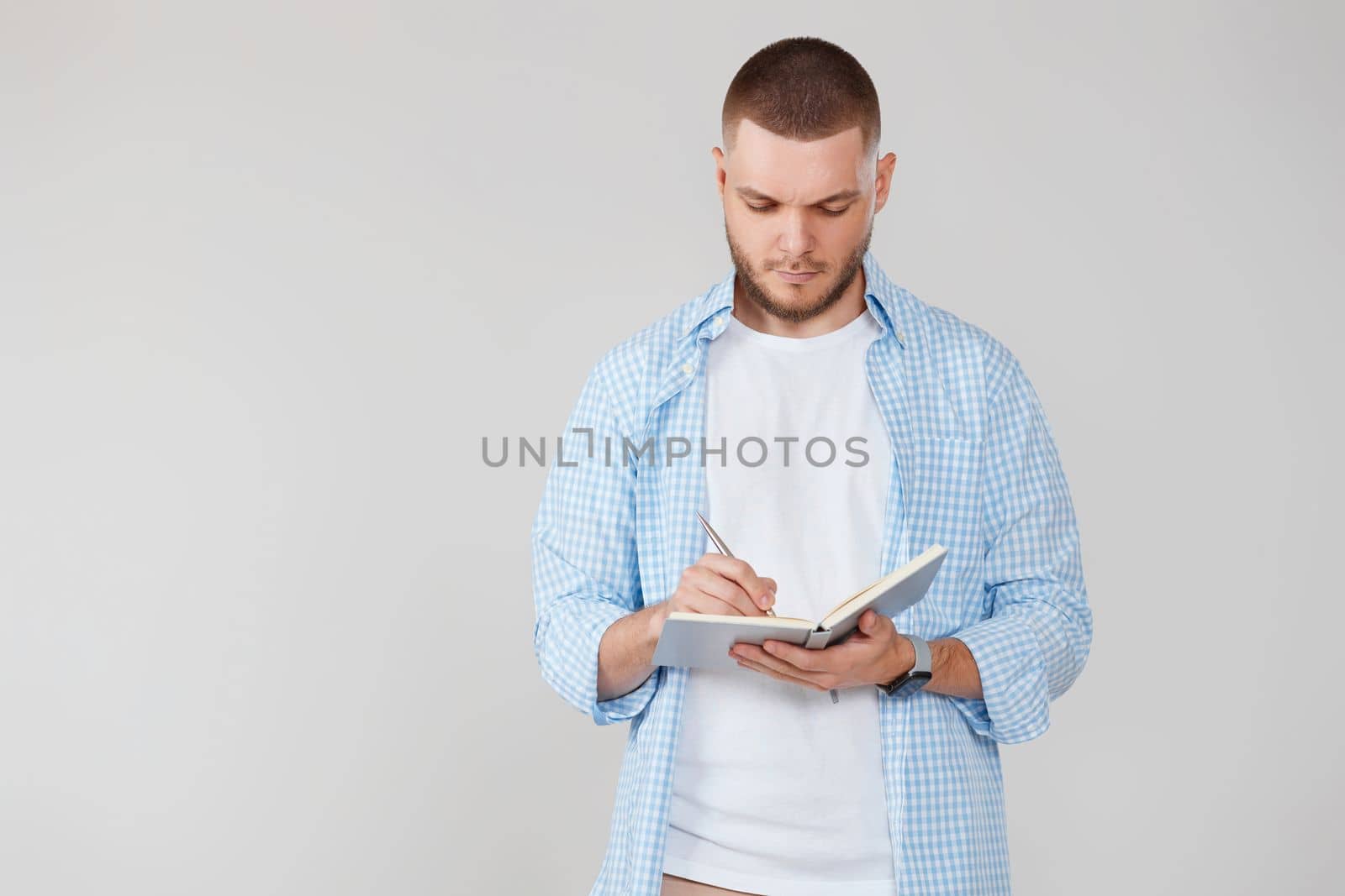 handsome man in casual blue shirt writing note in notebook