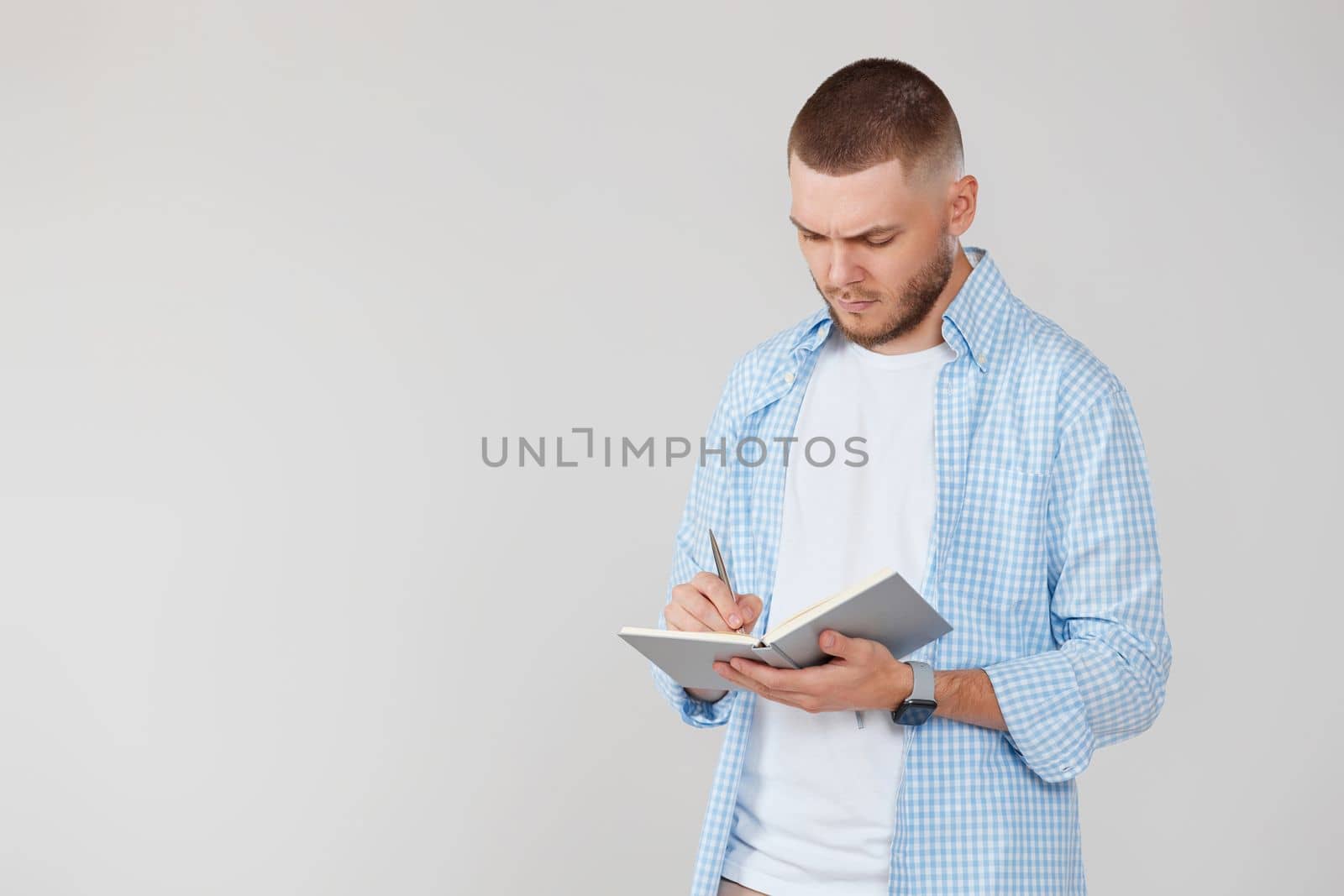 confident handsome man in casual blue shirt writing note in notebook. space for text