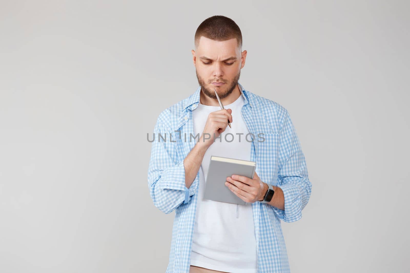 serious handsome man in casual blue shirt holding notebook, planning or thinking about question