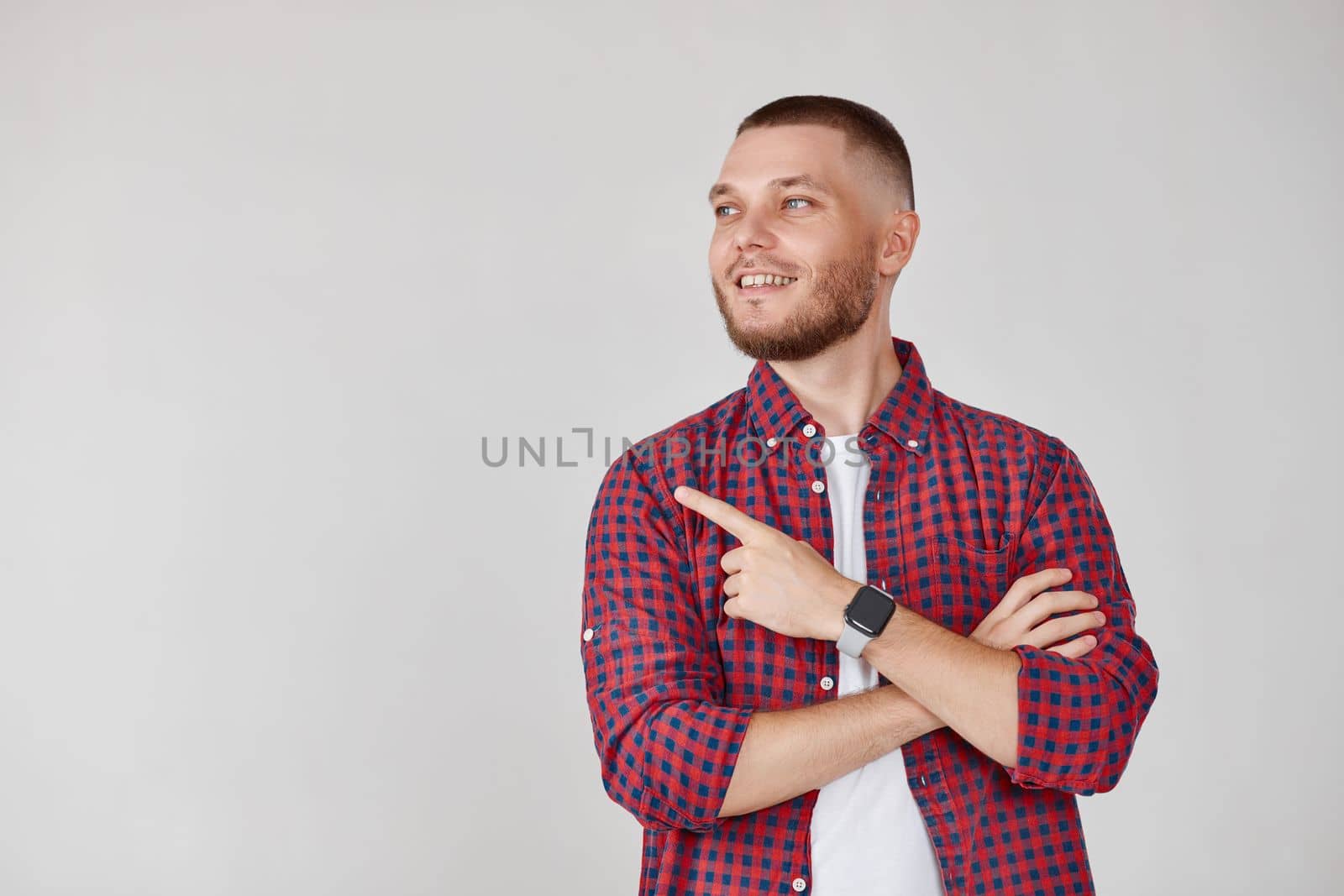 Young smiling handsome bearded man pointing to the side to present a product isolated on gray background