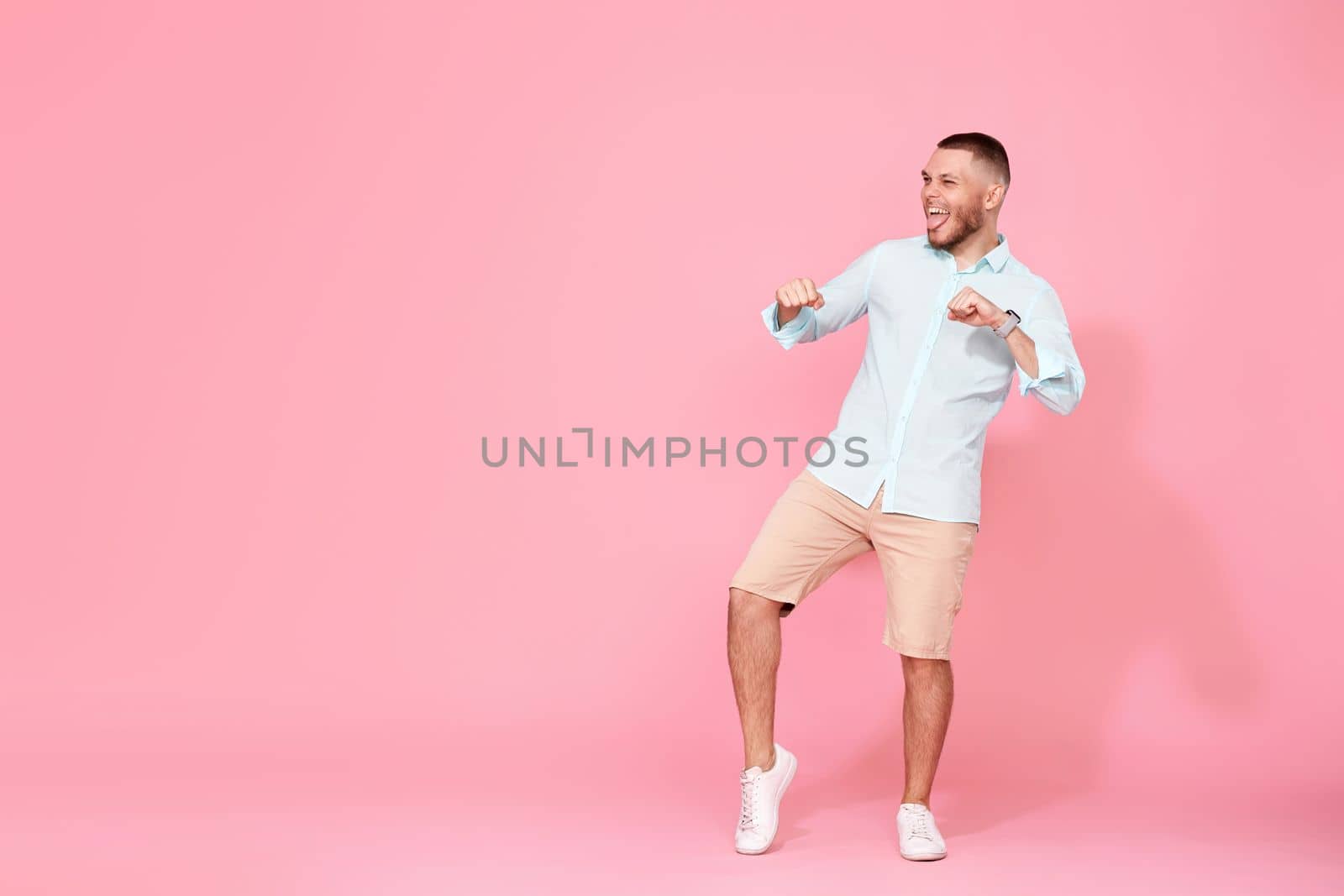 handsome smiling man in blue shirt dancing isolated on pastel pink background. Full length