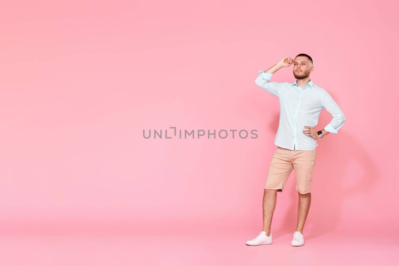 positive dreamy thoughtful young man looking at the copy space and thinking isolated on pink background. Full length
