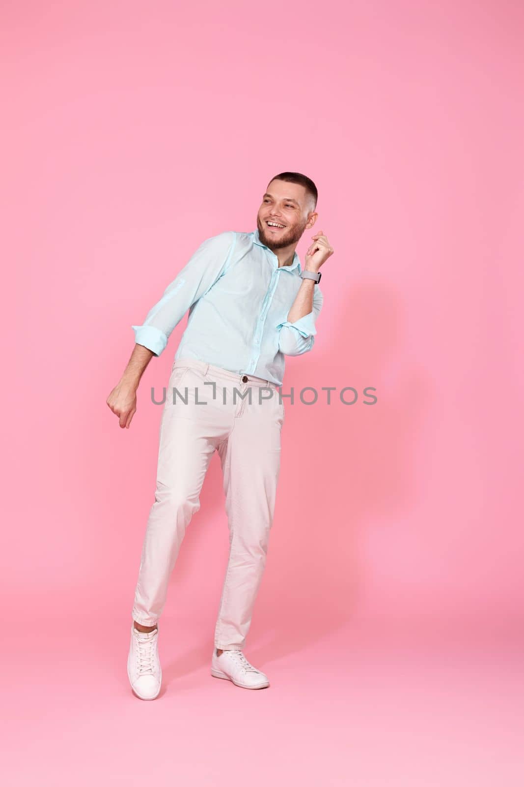 handsome smiling man in blue shirt dancing isolated on pastel pink background. Full length