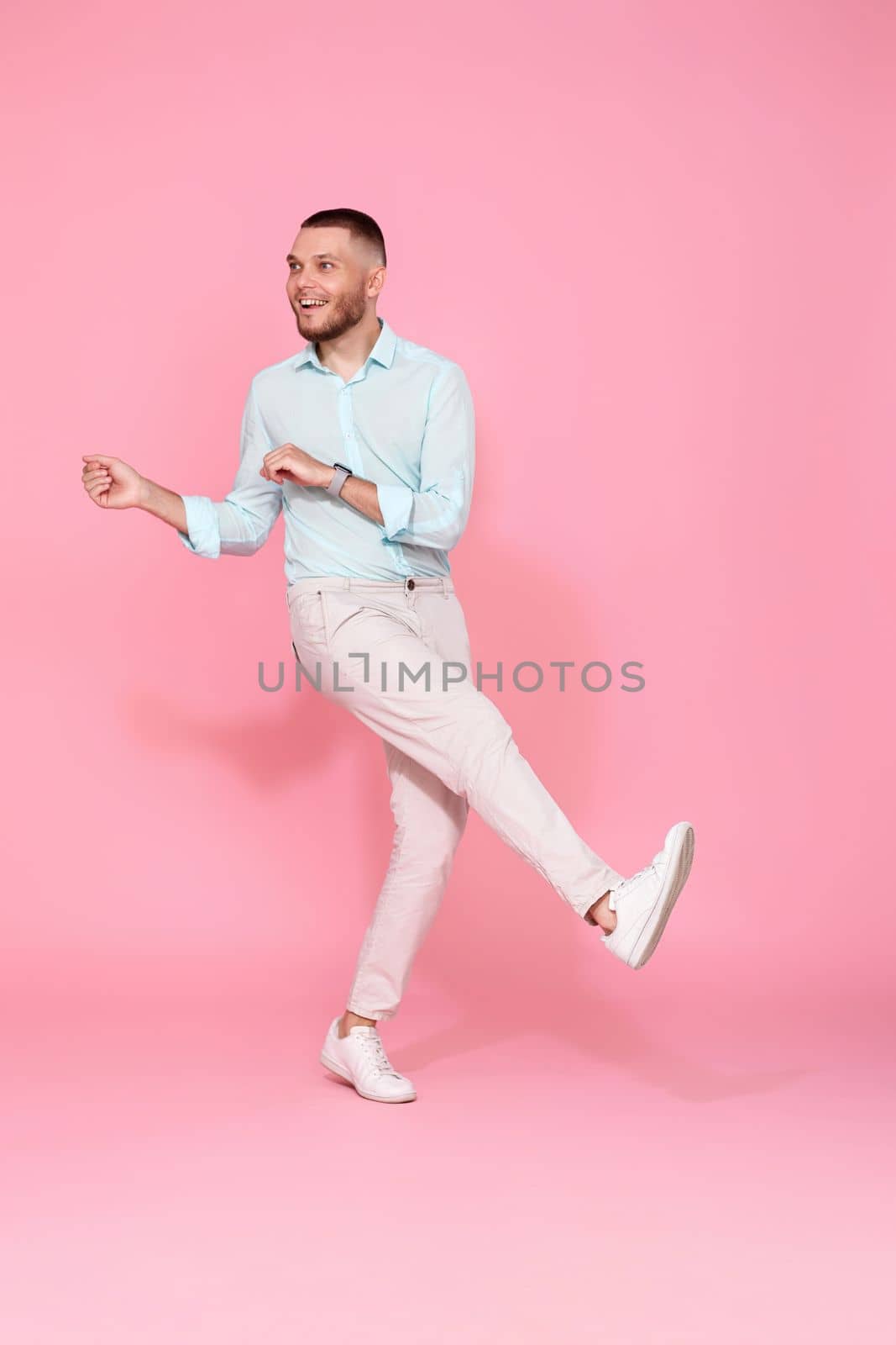 handsome smiling man in blue shirt dancing isolated on pastel pink background. Full length