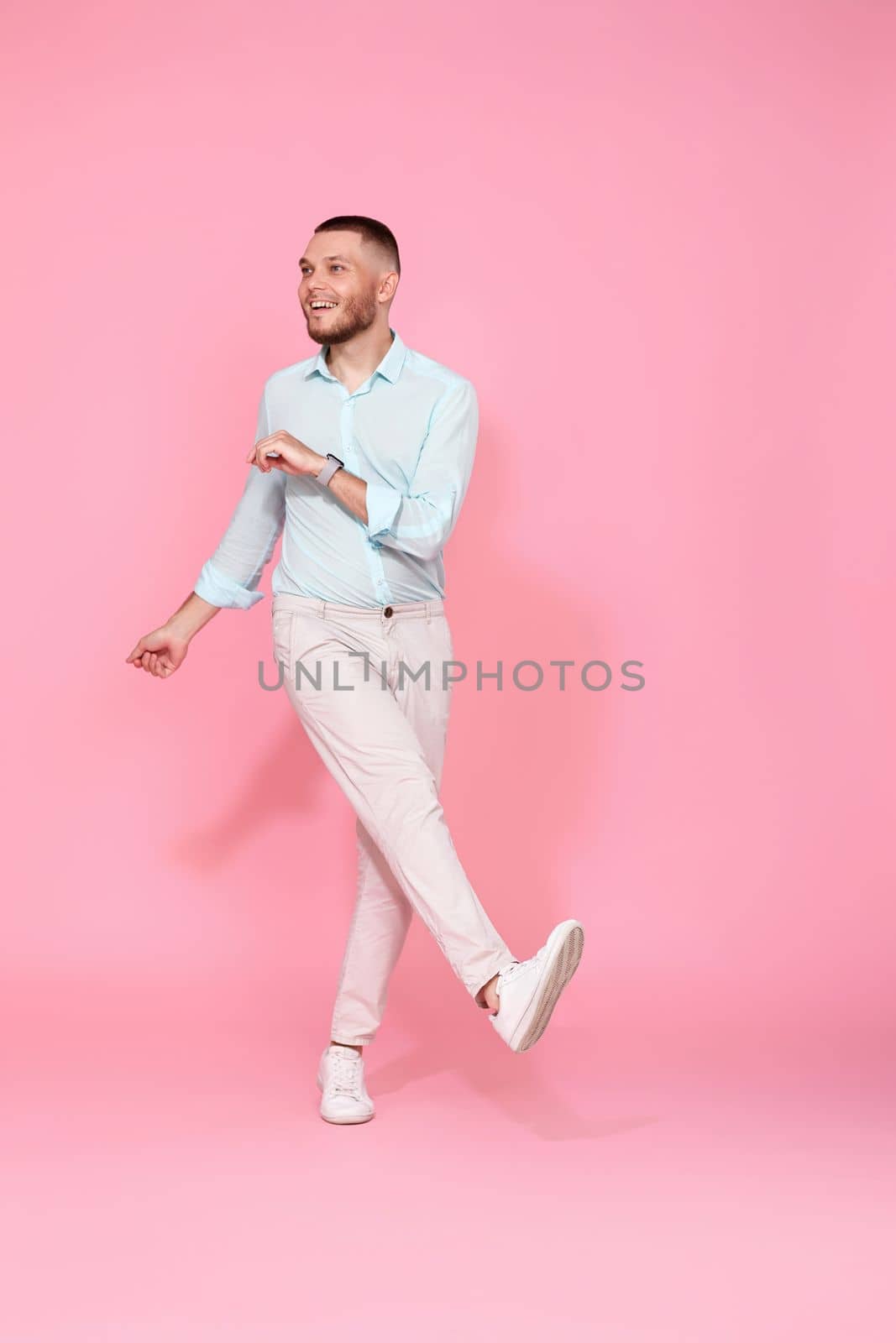 handsome smiling man in blue shirt dancing isolated on pastel pink background. Full length