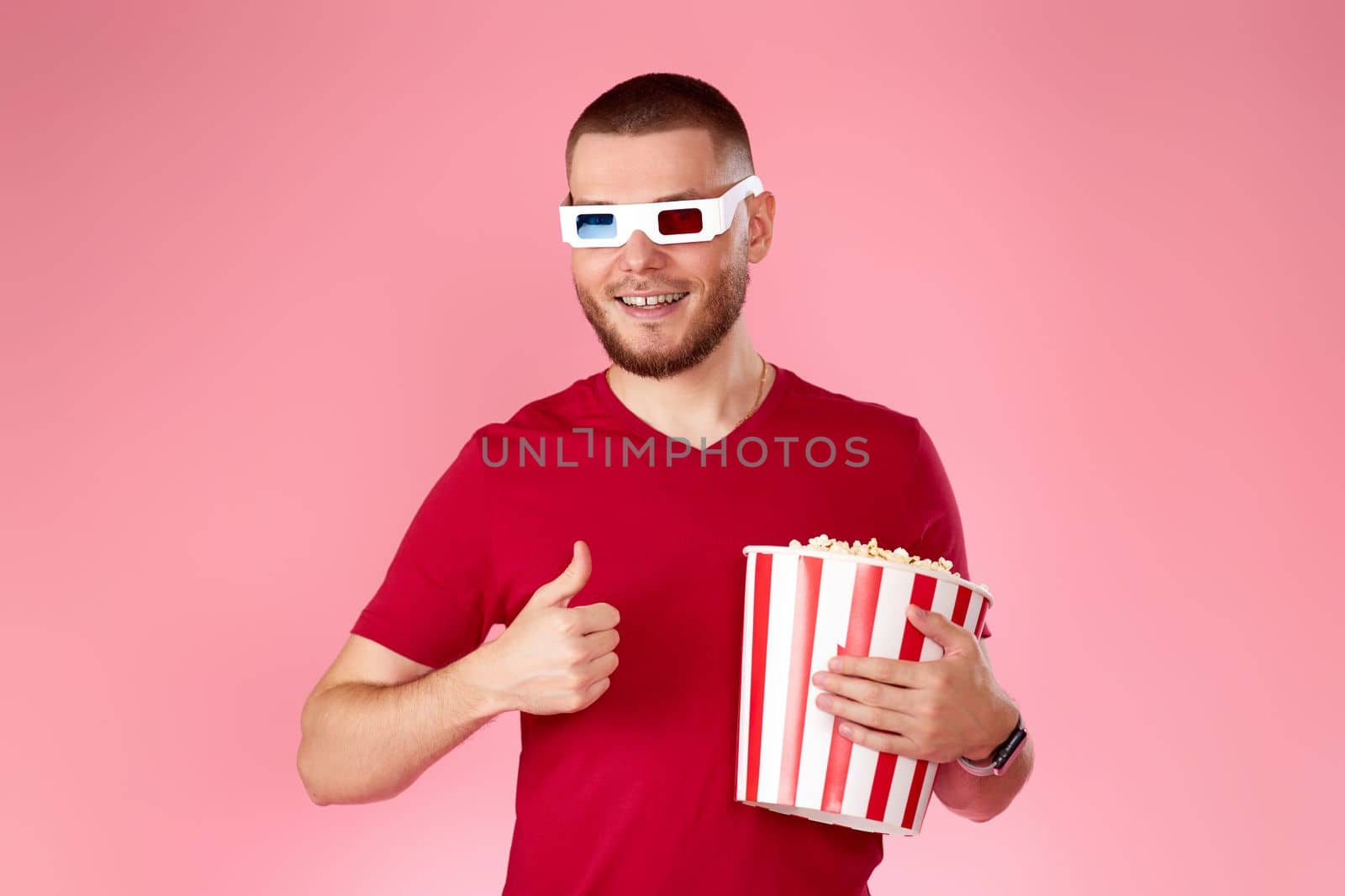 Young caucasian man eating popcorn and showing ok gesture on pink background