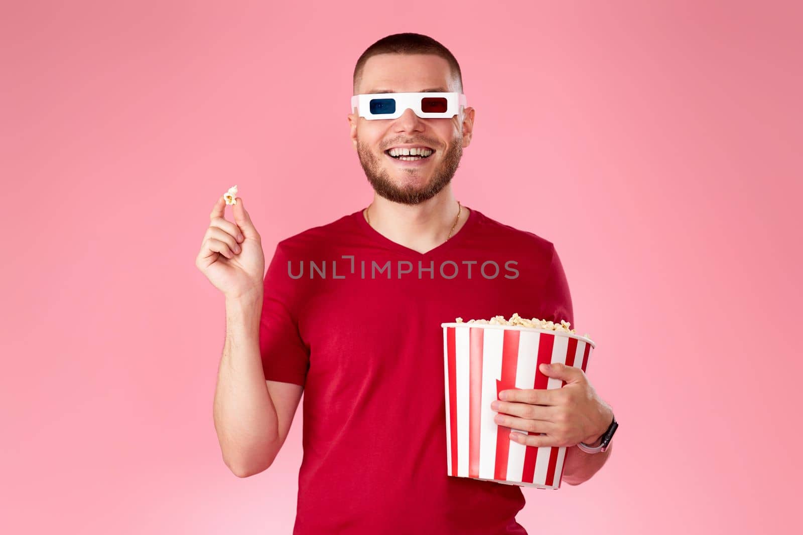 happy caucasian man in 3d glasses eating popcorn on pink background