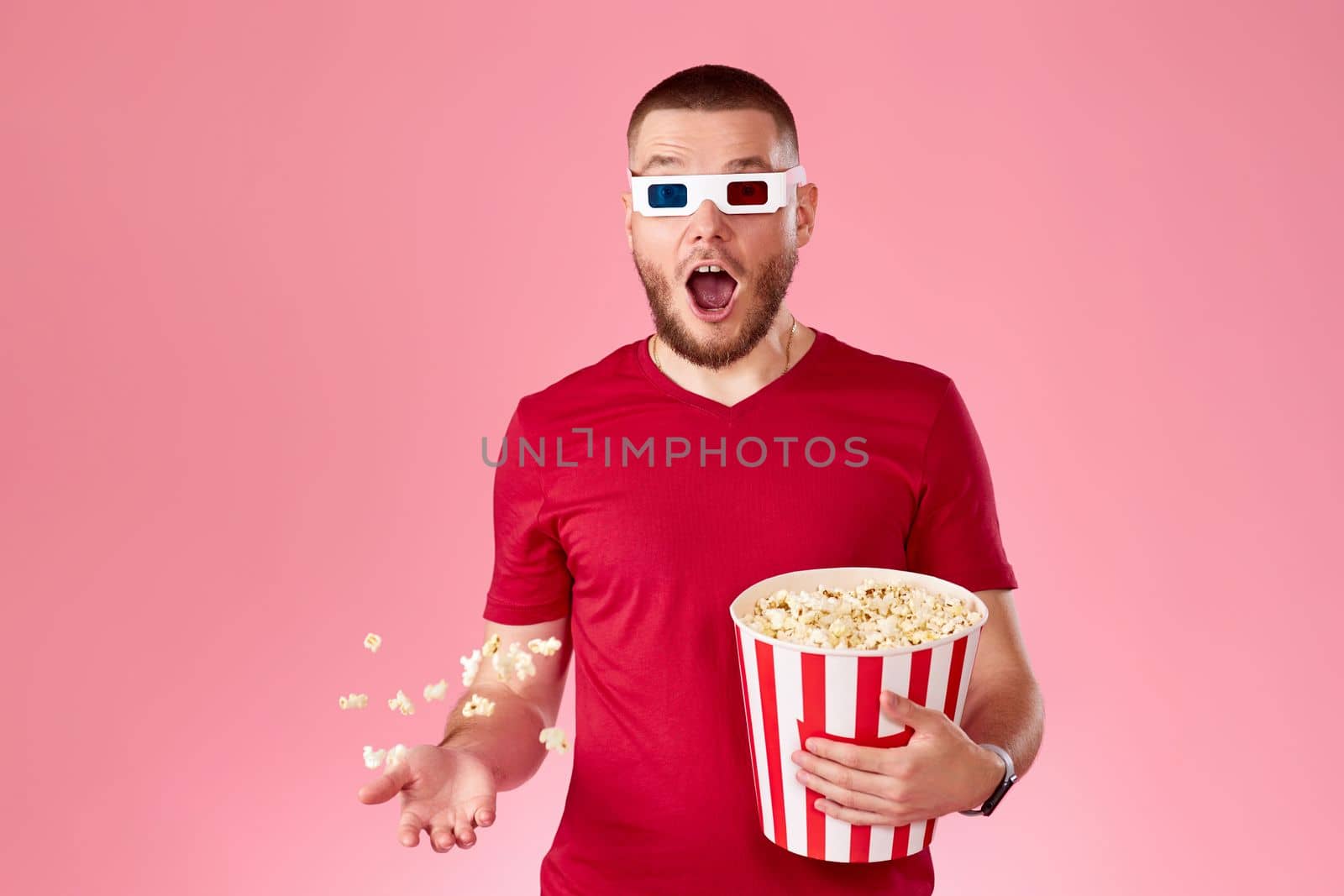 surprised man in 3d glasses throwing up and eating popcorn on pink background