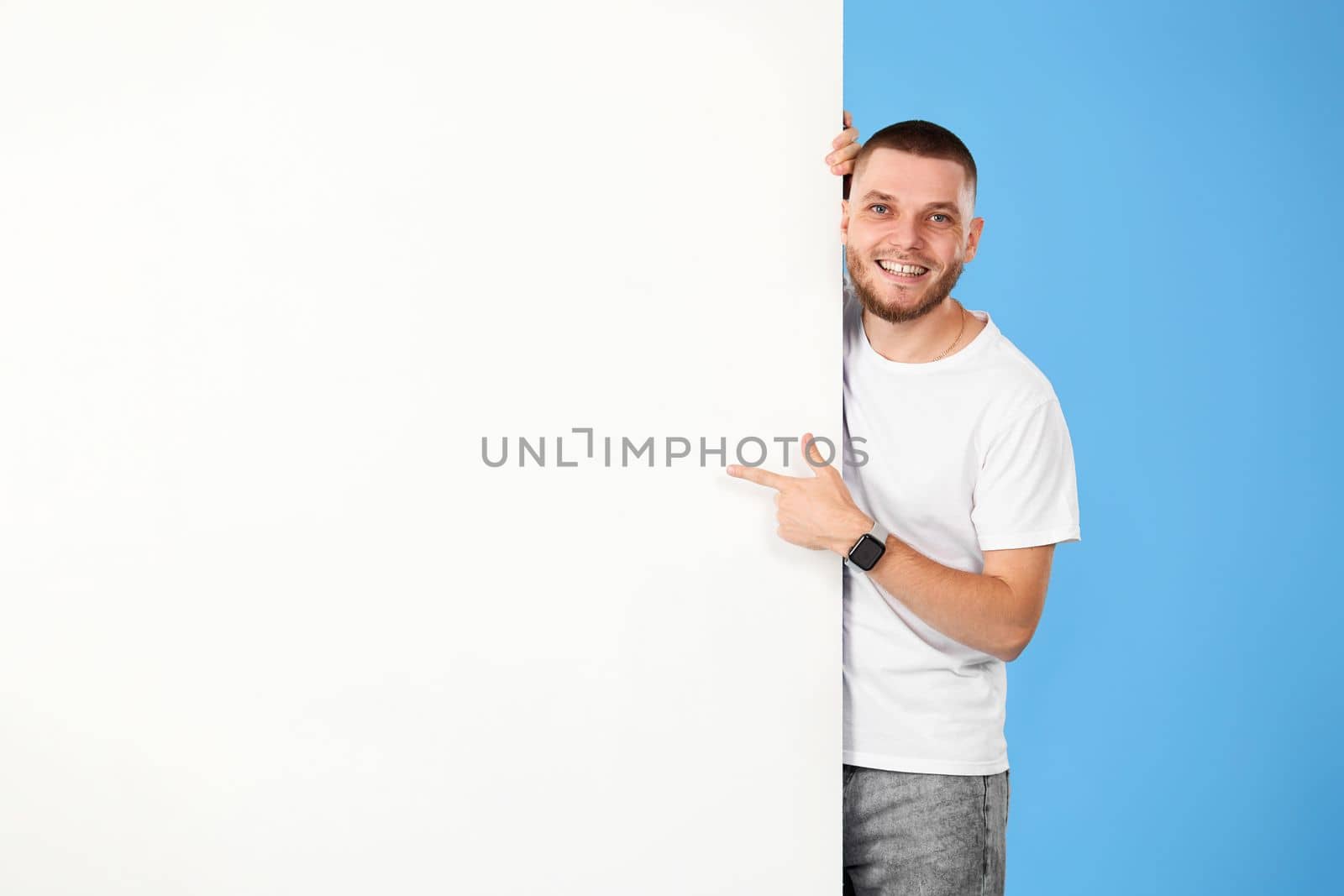 Portrait of cheerful bearded man pointing at blank advertising board with empty copy space isolated on blue background. mock-up
