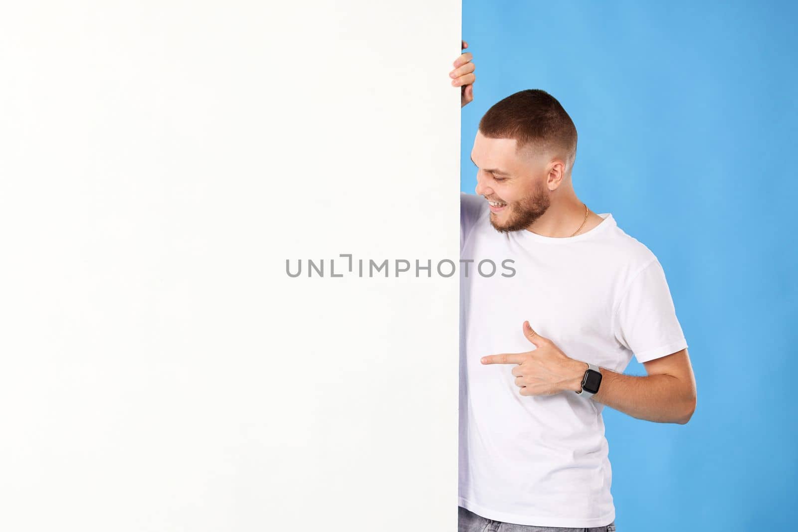 Portrait of friendly man point finger empty space banner isolated on blue background. mock-up