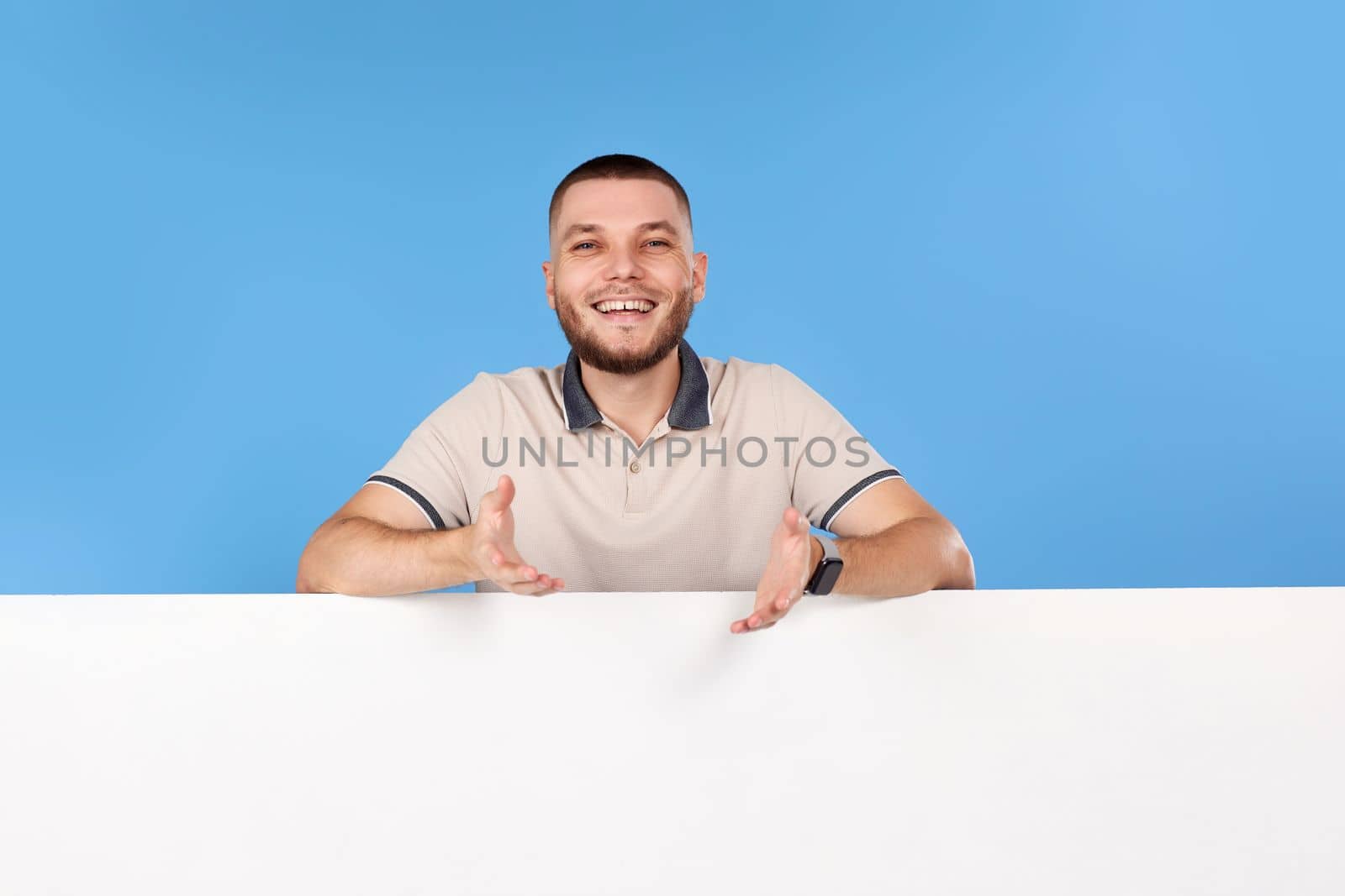 Portrait of cheerful bearded man leaning on empty placard for advertisement with empty copy space on blue background
