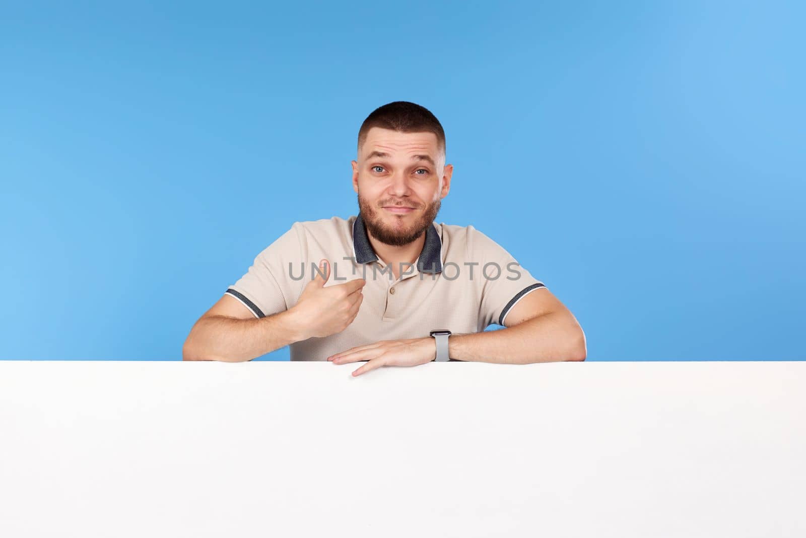 man pointing at himself and shrugging confused with board with empty copy space isolated on blue background