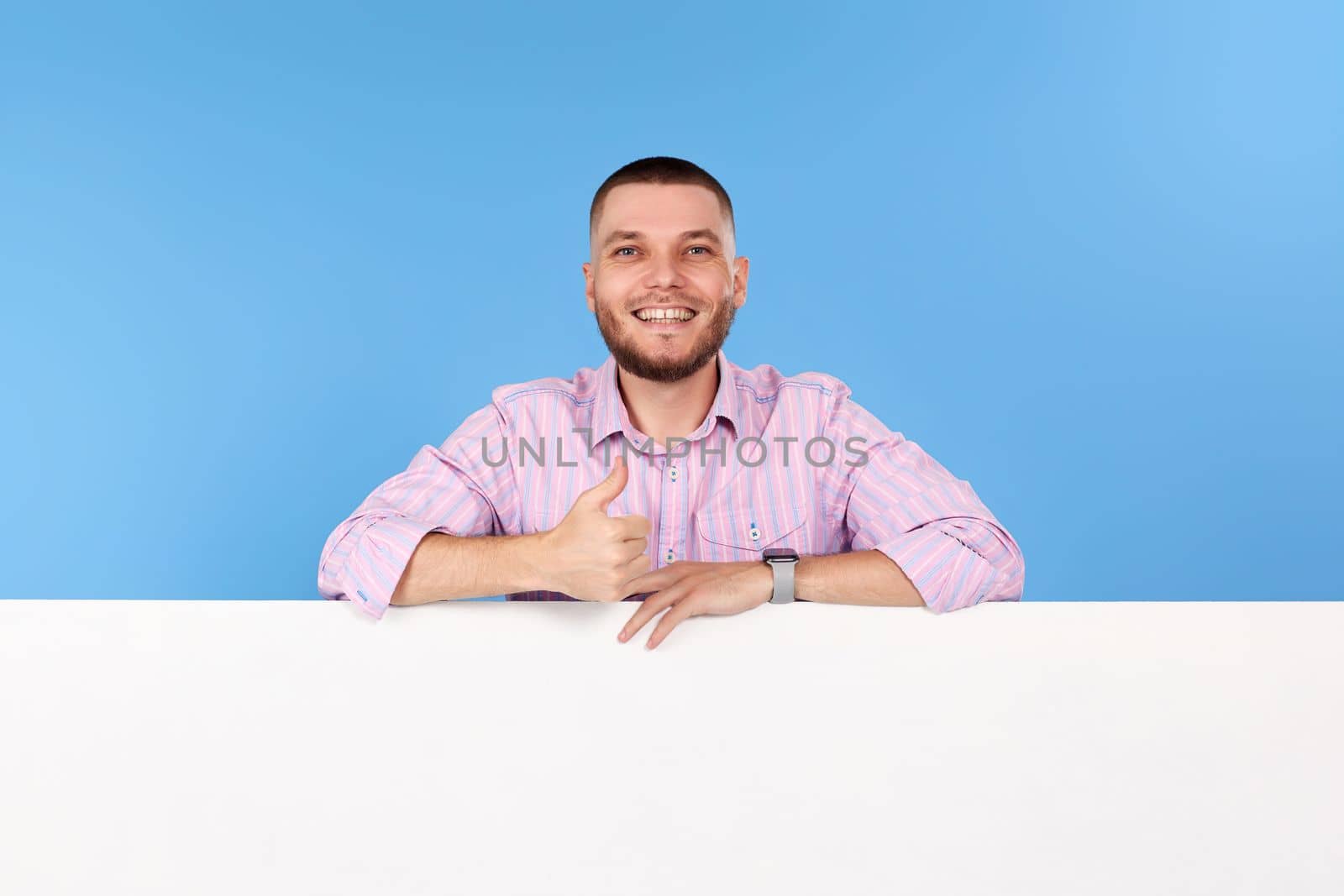 Portrait of cheerful bearded man holding board with empty copy space and showing thumb up isolated on blue background