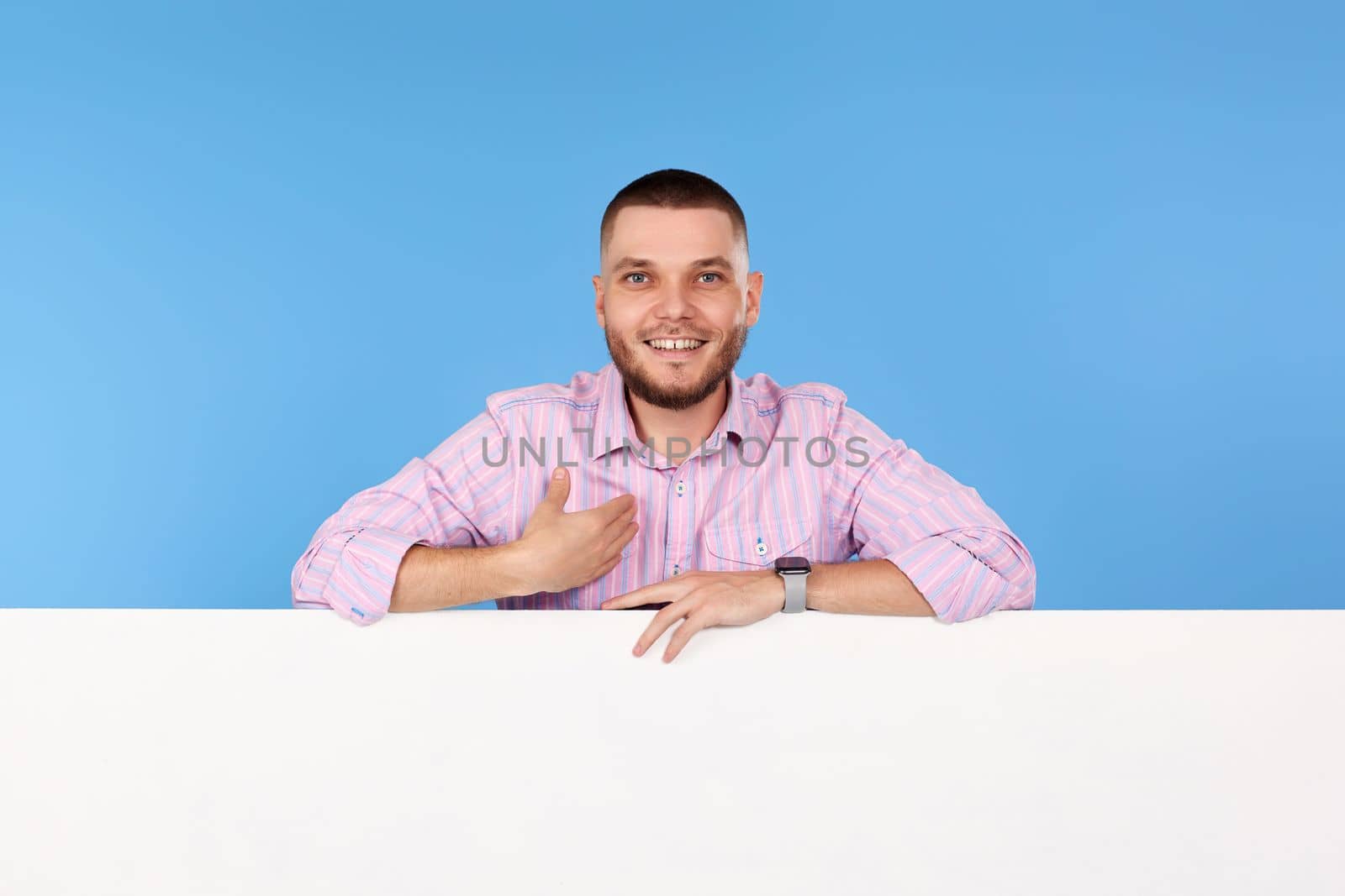 smiling man pointing at himself and placard with empty copy space isolated on blue background