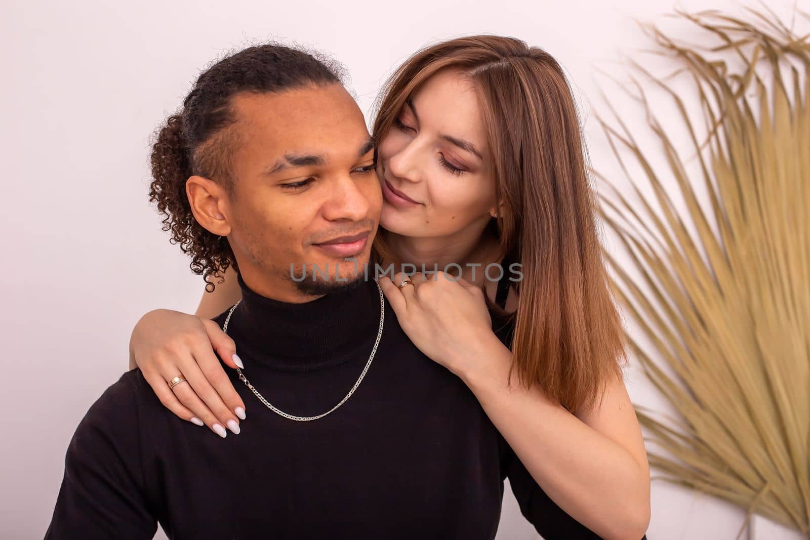 Portrait of multiracial couple, in black clothes, near the wall in the room. by Zakharova