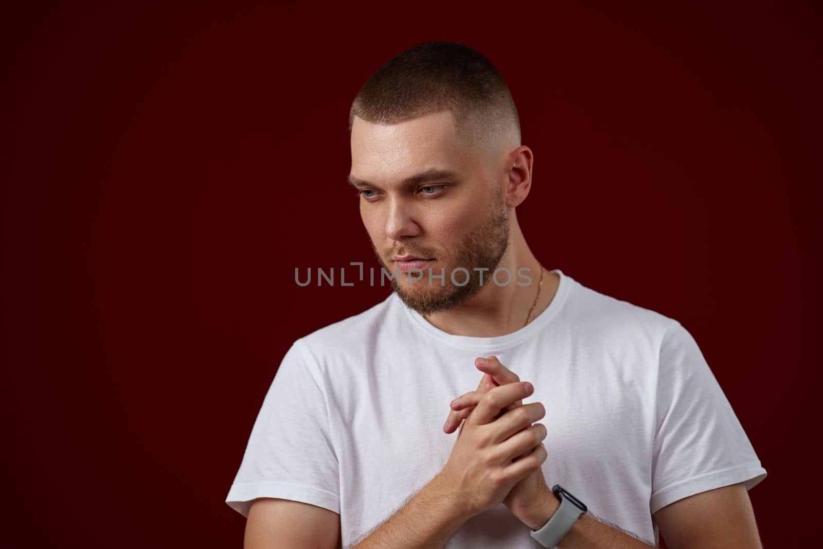 young handsome man in a white t-shirt thinks about something on a red background