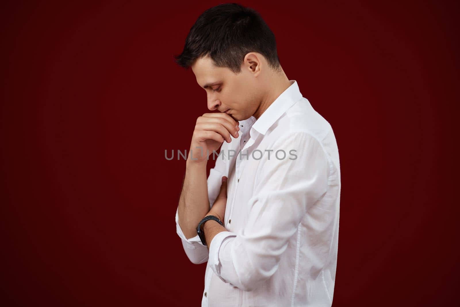 thoughtful man holding arms folded, touching chin with hand and looking down on red background