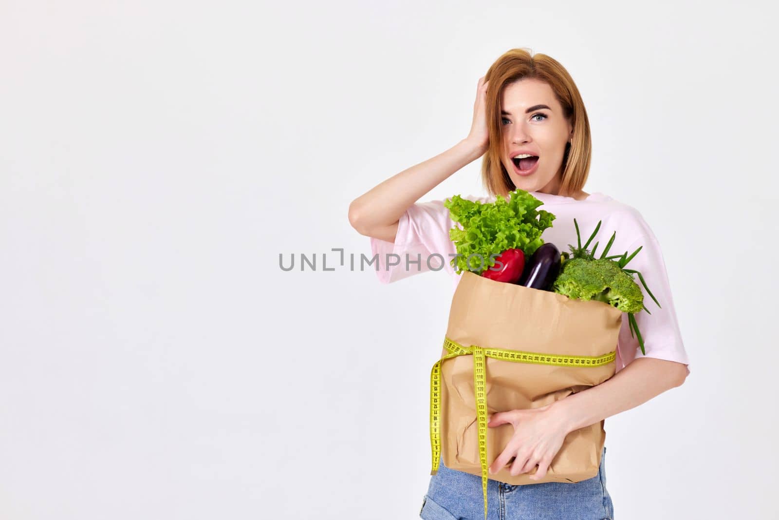 slim beautiful girl holds paper bag with vegetables and measuring tape isolated on white background. copy space. healthy food for diet