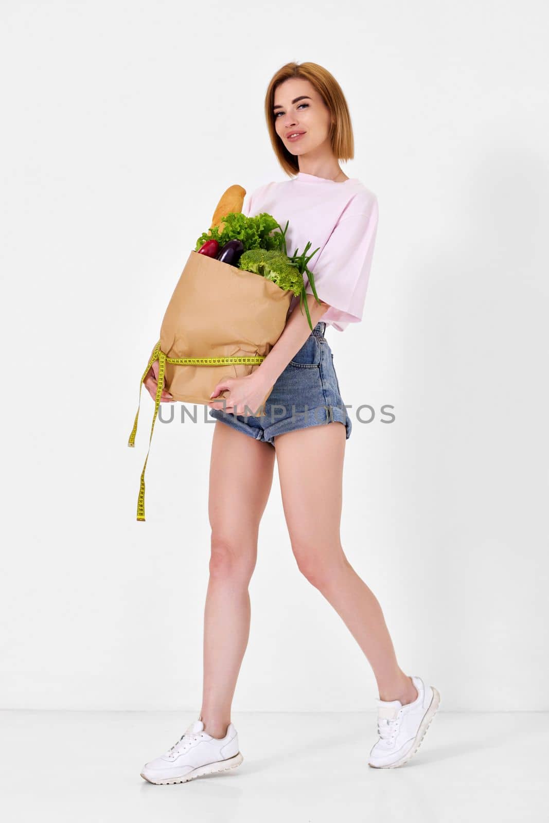 young sporty woman holding a shopping bag full of groceries and measuring tape. healthy food for diet. full length
